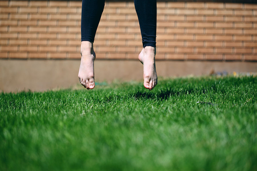 A pair of feet jumping off a lush, green lawn. Photo by Sharon McCutcheon.