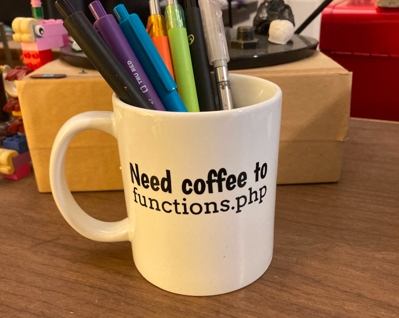 Mug with pens that reads, "Need coffee to functions.php"