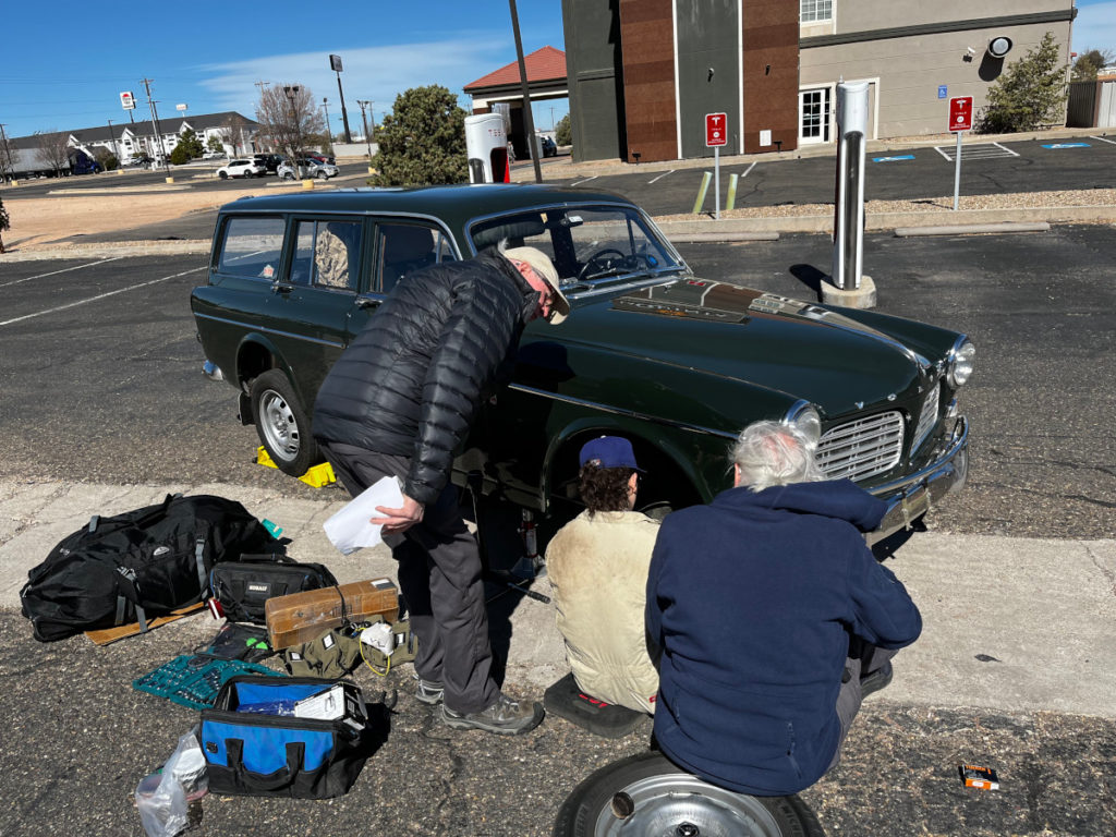 People gathered around a green 1967 Volvo in a parking lot